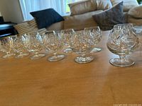 Twelve cut crystal brandy snifters arranged in a line on a wooden table, showing two styles with faceted diamond cut patterns, clear crystal glassware