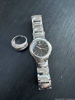 Photo of the Seiko wristwatch and silver-tone gemstone ring together on a black surface, showing overall look and size