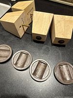 Four light blonde wood furniture feet each with an attached threaded metal screw and four round brown plastic caster cups arranged neatly on a black surface.