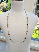 Gold-tone station necklace displayed on a mannequin bust near a window showing clear and black stones alternating along thin chain.