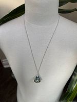 Full view of the pendant necklace on a mannequin bust showing the silver-tone chain and light blue/clear teardrop crystal pendant.
