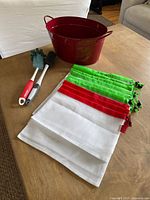 Full view of the red bucket, two bottle brushes (one red, one white handle) and nine colorful mesh shopping bags laid flat on a wooden table.