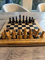 Top-down photo of the full chess set displayed on wooden table, showing board with both light and dark pieces arranged in starting position.