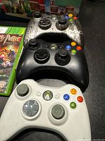 Three Xbox 360 controllers stacked with an Xbox game case showing Harry Potter cover insert