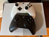 Top-down view of white console top and perforated vent area with one white and one black controller atop.