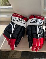 Pair of Reebok Cougars hockey gloves in black, red, and white, showing front and top padding and logos.