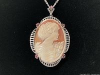 Frontal view of oval carved shell cameo pendant in filigree silver frame with pink stones