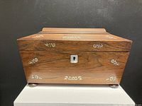 Front view of rosewood tea caddy showing sarcophagus shape, mother of pearl inlay floral patterns, and central keyhole.