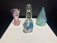 Group shot of four small art glass vases on white pedestal against black background.