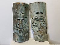 Pair of carved and painted cedar masks leaning against a wall, showing both masks side by side