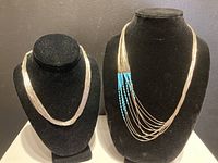 Front view of a pair of liquid silver necklaces on black velvet busts showing the 10-strand and 30-strand necklaces.