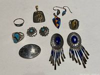 Full view of the 11 pieces of Southwest silver jewelry arranged on white background, showing rings, earrings, pendants, and brooches with turquoise and other stones