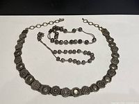 Full view of the Bedouin belt laid out in a circle alongside two sets of prayer beads.