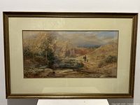 Framed antique watercolour painting showing a rural landscape with figures and old stone building under a cloudy sky.