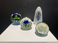Group of four art glass paper weights displayed on white surface with black background