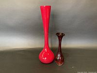 Photo showing both the tall red cased glass vase and the shorter reddish-brown Aseda glass vase side by side against a plain background.