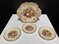 Four dishes arranged together showing fruit design and gold trim