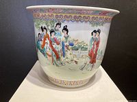 Front view of the porcelain jardiniere showing multiple hand-painted female figures in traditional clothing in a garden scene with bamboo and painted border designs.