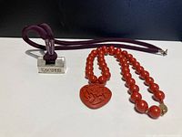Both necklaces shown flat including the Chinese silver pendant on fabric cord and cinnabar bead necklace with carved pendant.