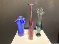 Set of three art glass vases on white pedestal against black background