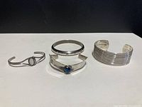 Four silver bracelets displayed together on white surface, showing different designs and sizes.