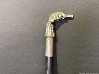 Close-up of the metal hand-shaped handle gripping the cane shaft, showing detailed sculpting and engraving.