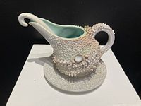 Front angled view of textured pottery sauce boat on matching plate.