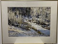 Front view of framed watercolor painting showing snowy creek scene