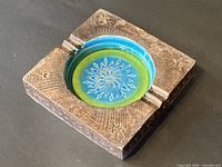 Square ceramic ashtray with a blue and green recessed circular center and intricate etched design