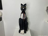 Front view of large black and white paper mache cat statue sitting upright with ribbon around neck.