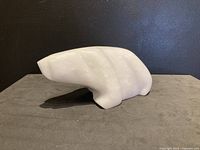 Left side view of the smooth white stone carved bear sculpture on a grey surface against a black background.