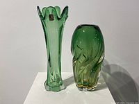 Pair of green Murano glass vases, taller vase has a flared, flower-like top and the shorter has an organic rounded shape with swirls.
