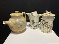Photo showing the teapot, cream jug, and sugar bowl from front angle to display shapes, colors and bird decoration on cream jug and sugar bowl.