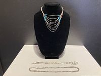 Three liquid silver necklaces displayed on a black jewelry bust and white surface.