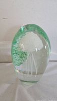 Front view of the clear glass oval paperweight with white jellyfish and green accents inside.
