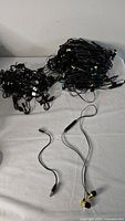Lot shows tangled collection of black charging cables and headphones with gold and black earbuds on white surface