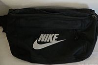 Front view of a large black Nike fanny pack showing the white Nike logo and zipper pocket.