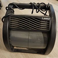 Front view of the black Lasko floor fan showing wave pattern grille and power cord wrapped on top handle.