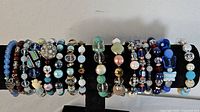 Wide shot of 13 assorted bracelets arranged on display stand showing various bead styles and colors mostly in blue and white tones
