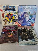 Four books arranged in a fan shape showing titles: JLA Justice League of America, The DC Comics Encyclopedia, Star Wars Vehicles & Vessels guide, and World War II history book.