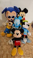 Six Mickey Mouse plush toys arranged in a pile showing different sizes and colors including a large blue Mickey with sunglasses.