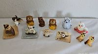 Photo showing 14 small owl figurines arranged in a row with varying colors and designs, some on tags.