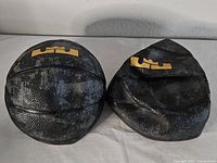 Two deflated mini basketballs, black with gold LeBron crown logo on top.