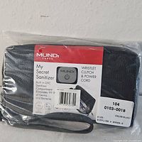 Photo of the Mundi wristlet clutch in new packaging showing the label describing the built-in UVC sanitizer and included power cord.