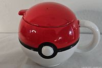 Front view of the red and white ceramic mug designed as a Pokeball with matching lid and white handle.