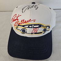 Front view of the white and navy baseball cap with embroidered yellow and black stock car with number 2 and red Rusty Wallace signature.