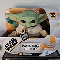 Front view of The Child plush talking figure in box packaging with blue alien accessory visible.