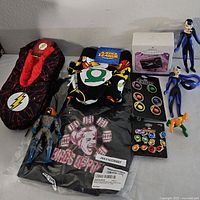 Overview of lot showing Flash slippers, DC Justice League and Harley Quinn shirts, superhero figurines, and jewelry sets