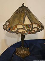 Full view of Tiffany style table lamp on dark surface, showing stained glass shade with floral and geometric patterns and bronze metal base.