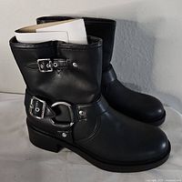Side angle view of one black ankle boot showing silver buckles and low heel.